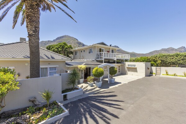 A two-story house with a balcony, a driveway, and a mountain backdrop.