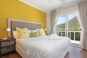 A bedroom with a large bed, a nightstand with a lamp, and a view of a mountain through a balcony.