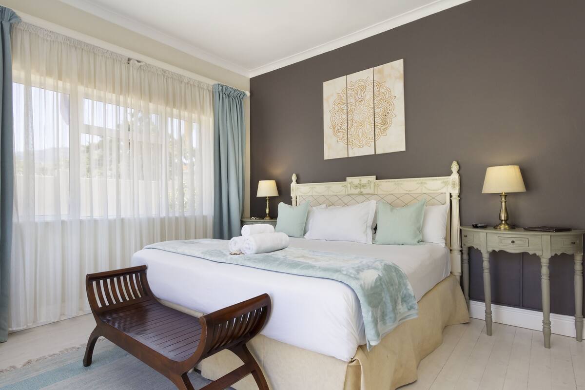 A neatly arranged bedroom with a large bed, two bedside tables with lamps, a bench, and a wall-mounted artwork.