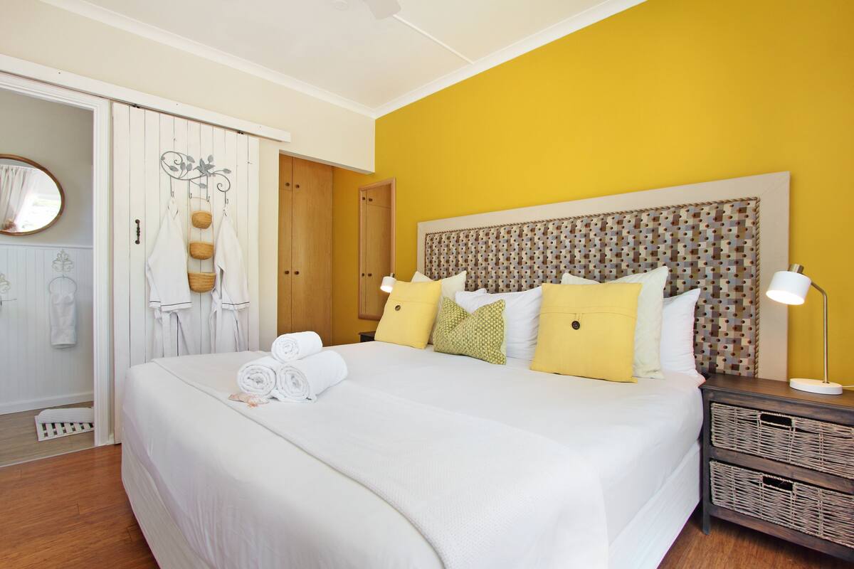 A neatly made bed with rolled towels, a headboard with a patterned design, and a bedside table with a lamp.