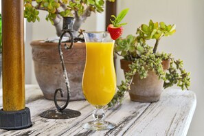 A glass of orange juice with a strawberry garnish on a rustic wooden table, surrounded by potted plants.