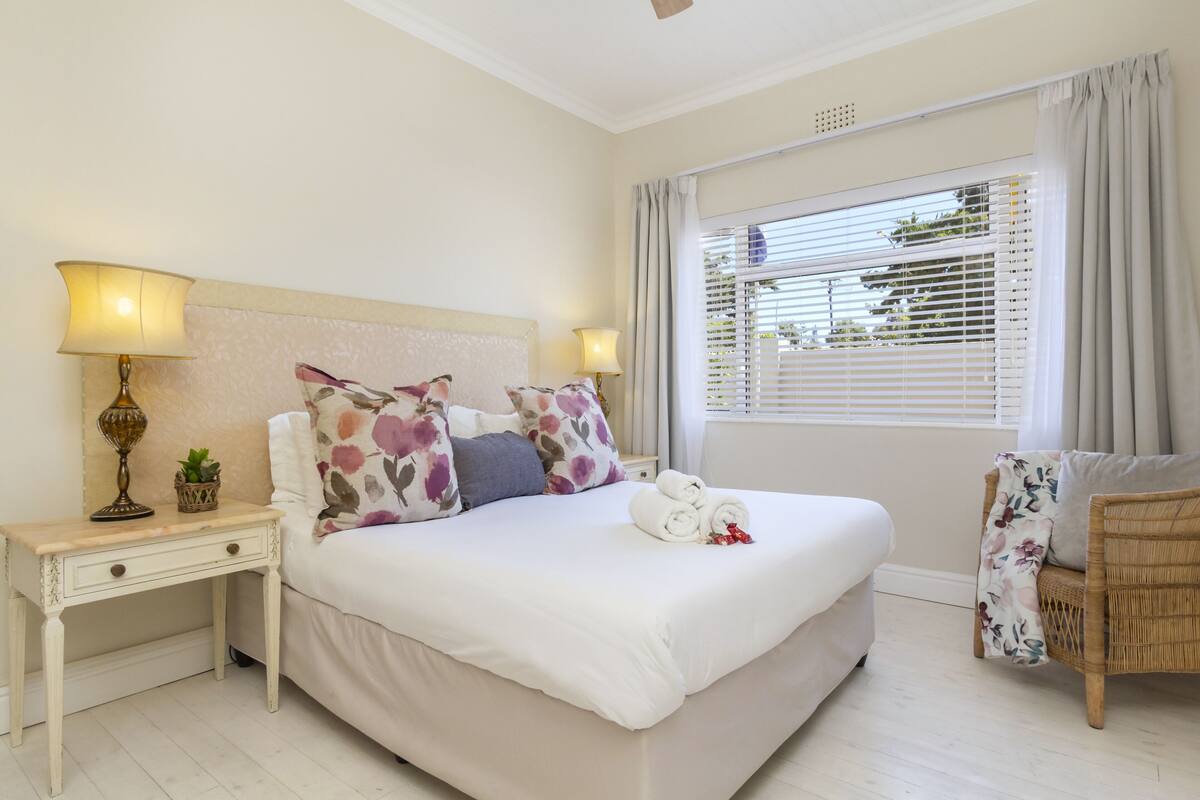 A neatly arranged bedroom with a bed, bedside tables, a lamp, a chair, and a window with blinds.