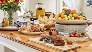 Mesa de café da manhã com doces, frutas e uma fruteira.