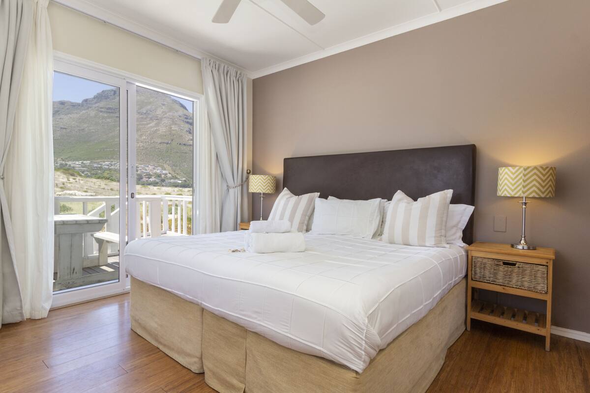 A bedroom with a large bed, a nightstand with a lamp, and a view of a mountainous landscape through a sliding door.
