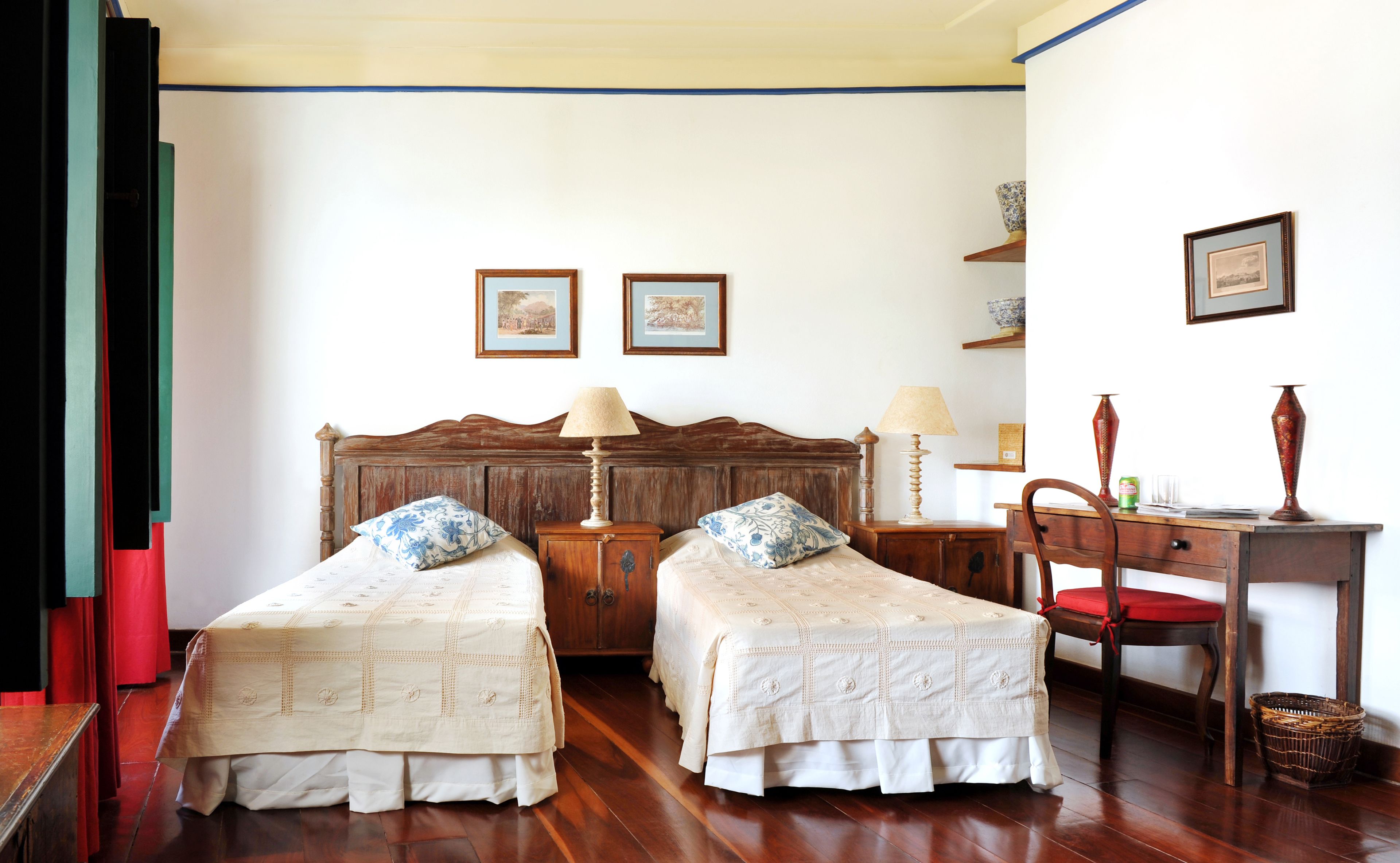 Una habitación con dos camas individuales, cabeceros de madera, un escritorio de madera con una silla y un estante pequeño con adornos.