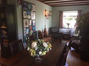 A dining area with a wooden table, chairs, and a floral centerpiece. There is a wall with various framed items and a bookshelf. - Hotel Heijenrath (Heijenrath)