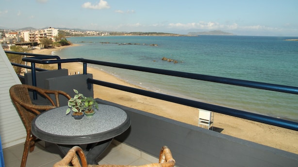 A balcony with wicker furniture, a round table, and a view of the beach and sea. - Hotel Danaos (Chania)