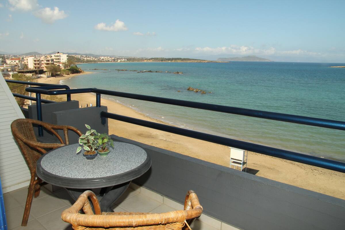 A balcony with wicker furniture, a round table, and a view of the beach and sea.