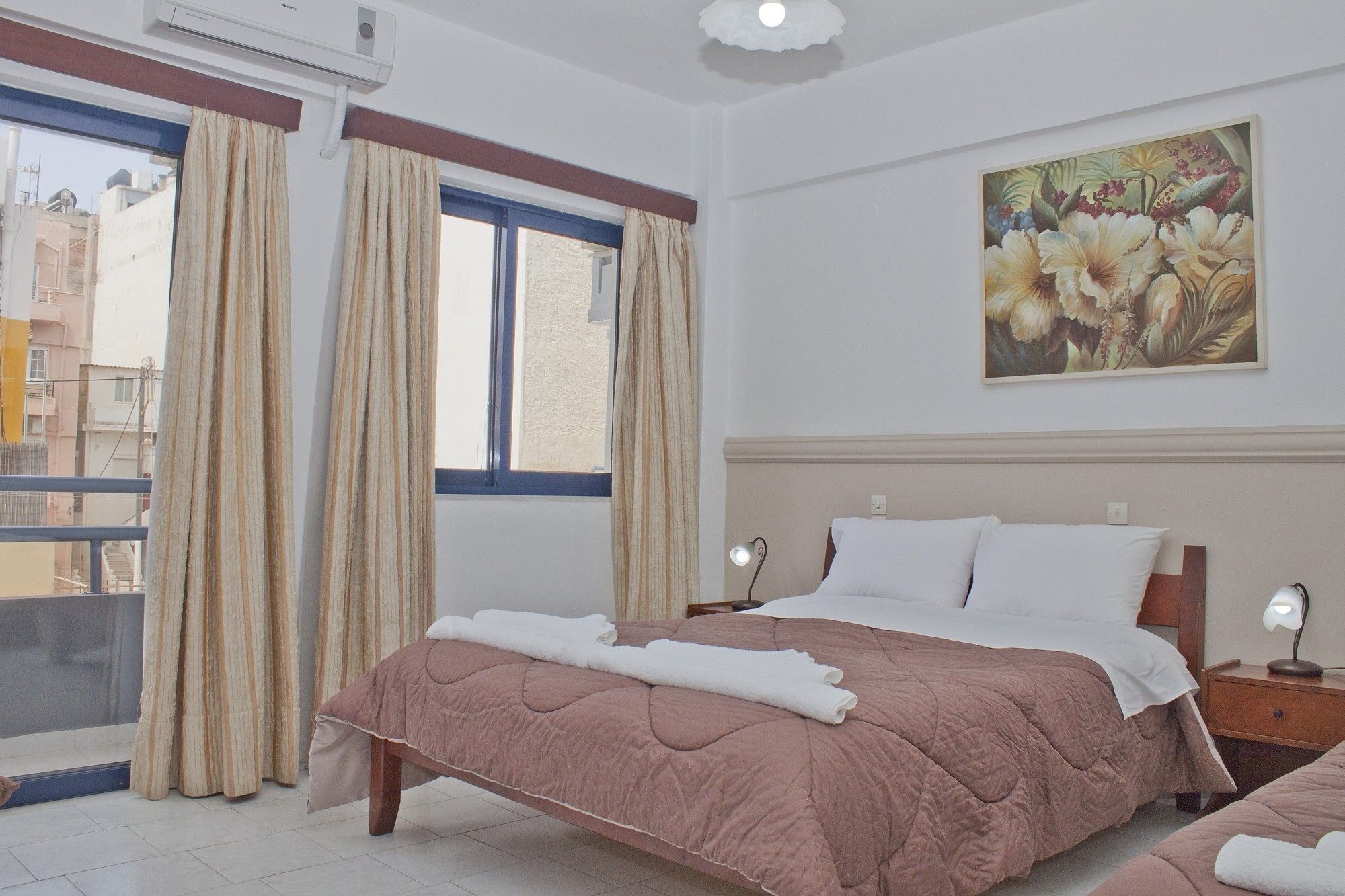 A hotel room with a bed, a nightstand, a lamp, a painting, and a window with curtains.