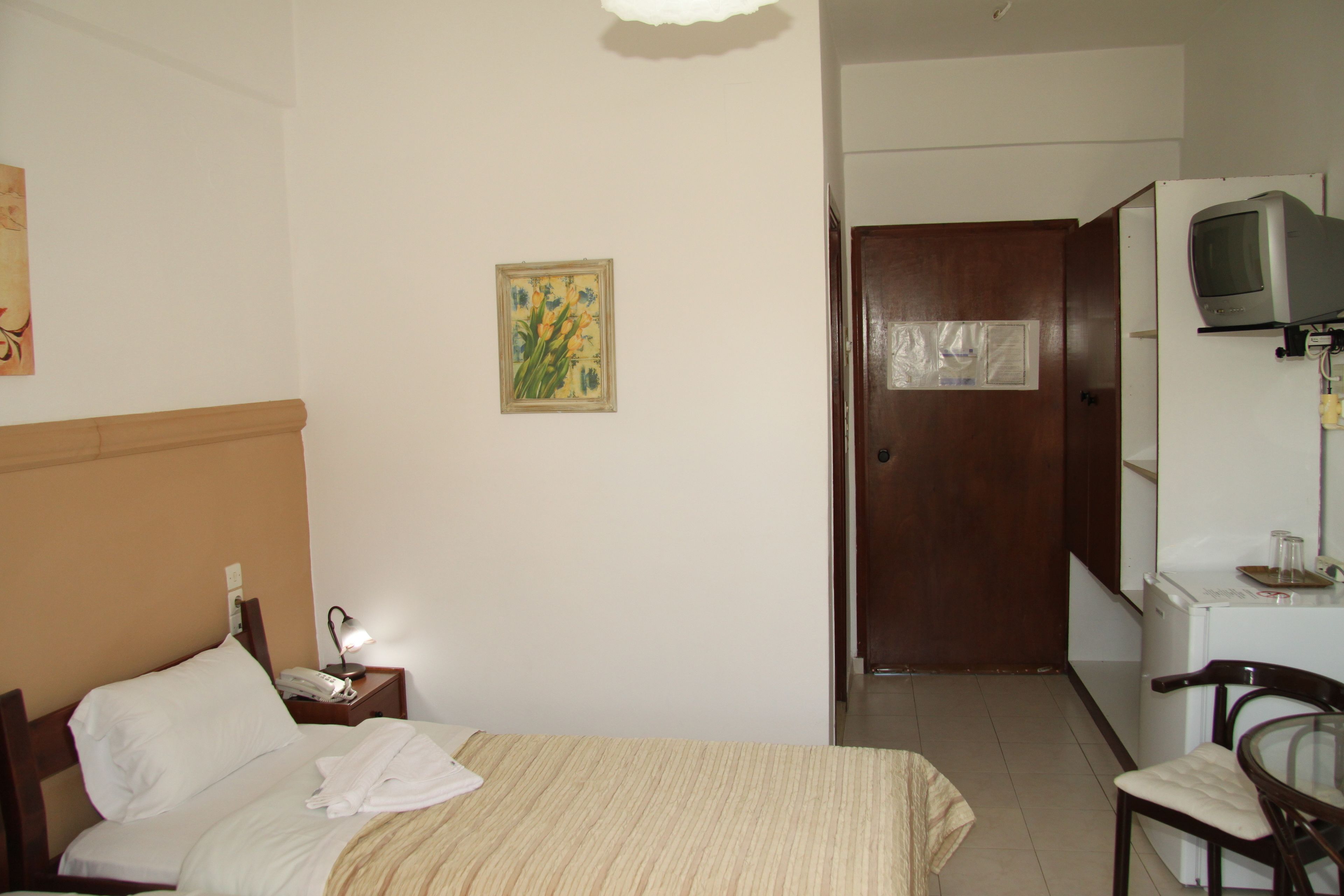 A hotel room with a bed, a bedside table with a lamp, a small table with a television, and a door leading to a bathroom.