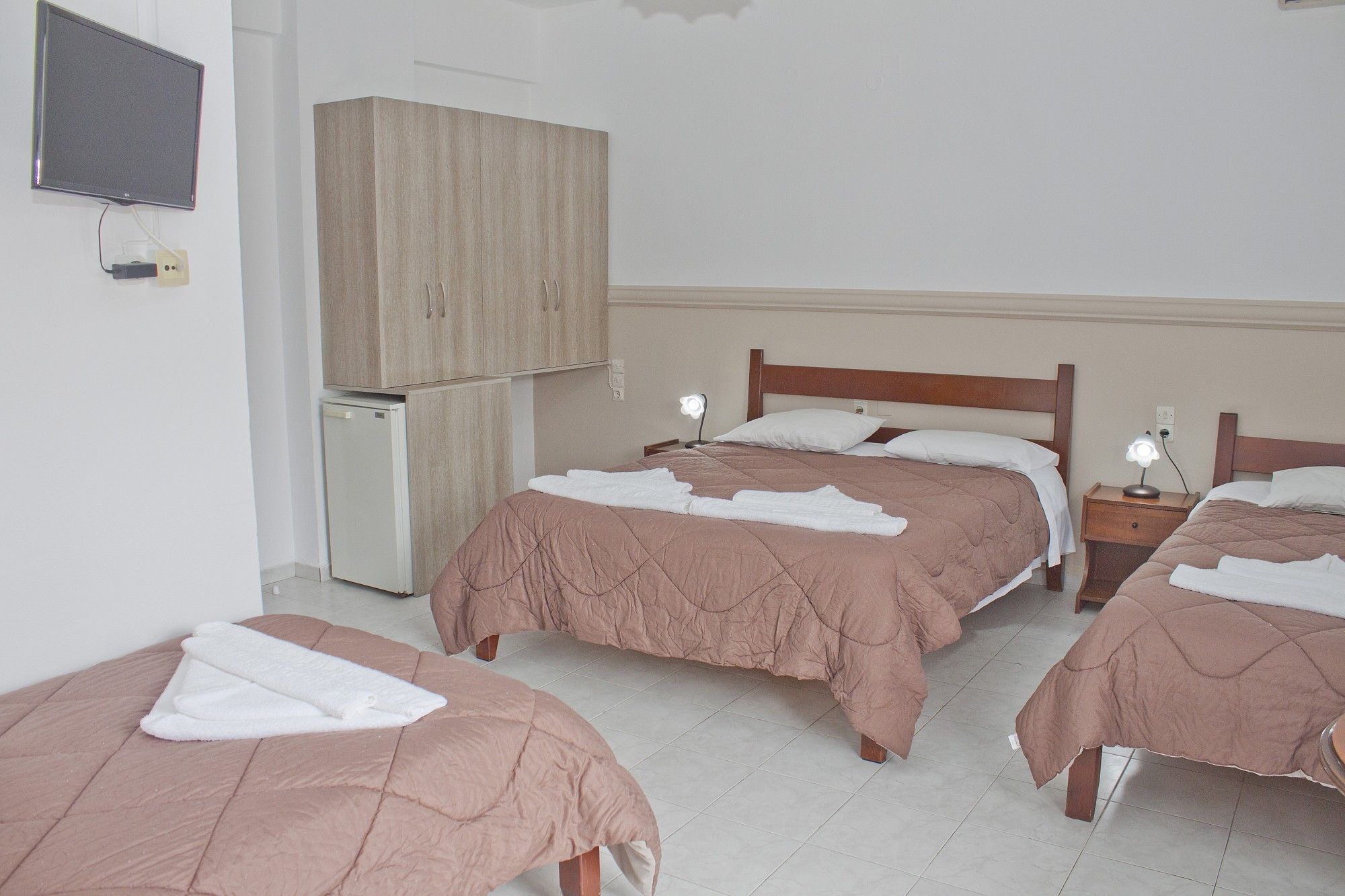A hotel room with three beds, a small refrigerator, and a TV mounted on the wall.