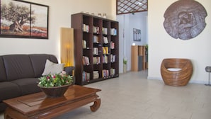 A living room with a dark brown sofa, a wooden coffee table with a flower vase, a large bookshelf, and a unique wooden chair. - Hotel Danaos (Chania)