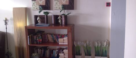 A room with a wooden bookshelf filled with books and decorative items, a floor lamp, and a wall-mounted painting.