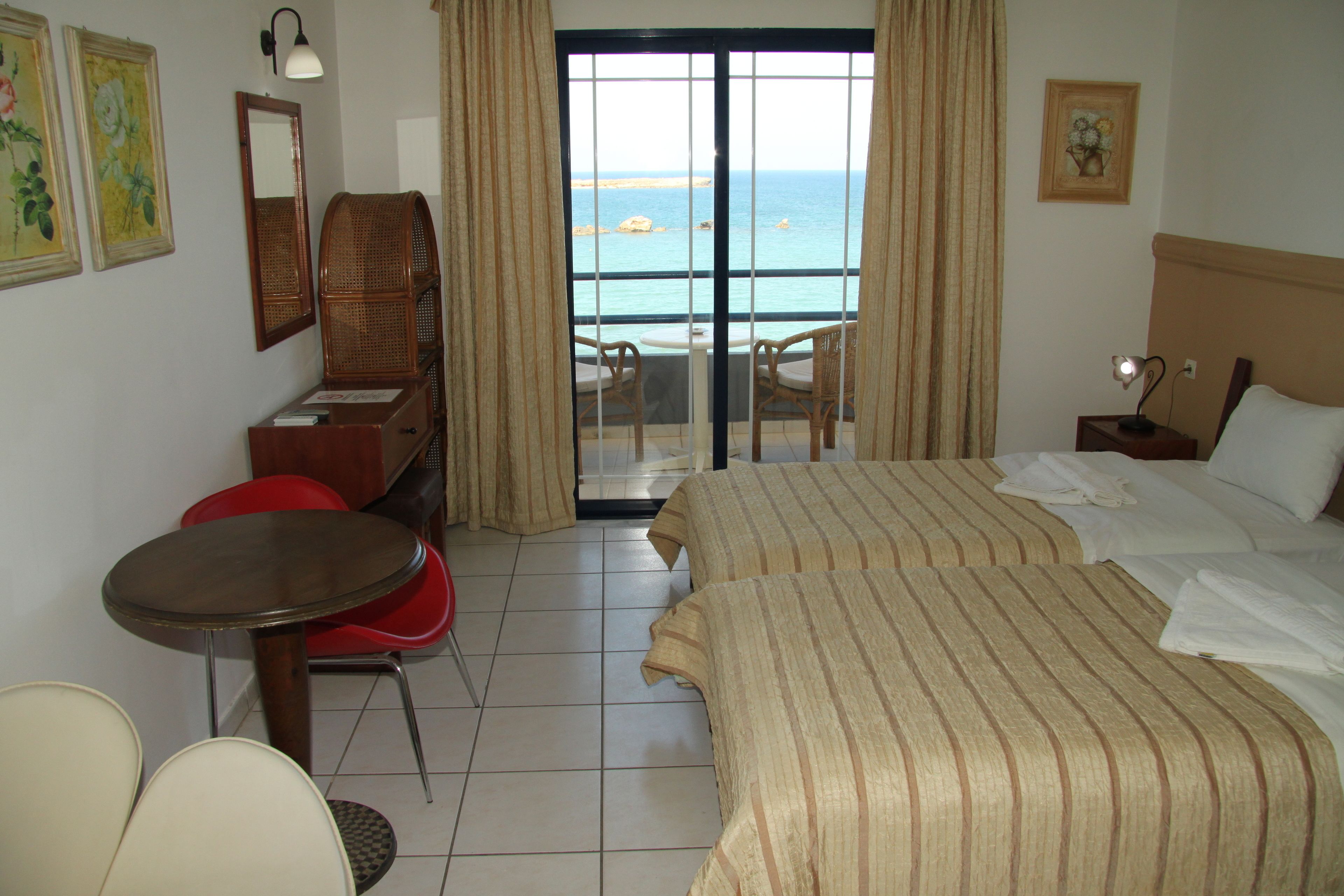 A hotel room with a bed, a desk, a chair, and a view of the sea through a glass door.