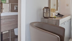A modern bathroom with a large mirror, a mounted TV, and a vanity with a sink and toiletries. - Hotel Danaos (Chania)