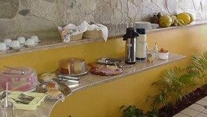 A breakfast bar with various food items, a coffee machine, and a fruit display. - Marambaia Apart Hotel (Natal)