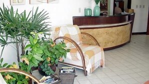 A reception area with a checkered chair, a reception desk, and potted plants. - Marambaia Apart Hotel (Natal)