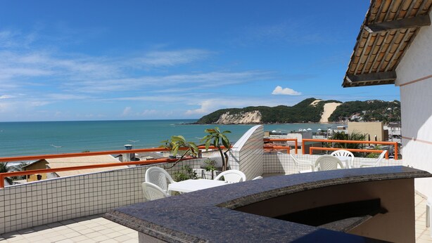 A terrace with a view of the sea, white chairs, and a tiled wall. - Marambaia Apart Hotel (Natal)