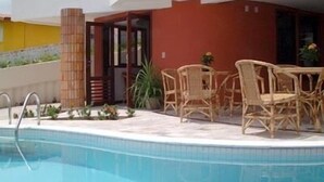 A swimming pool with a tiled edge, a wooden fence, and wicker furniture. - Marambaia Apart Hotel (Natal)