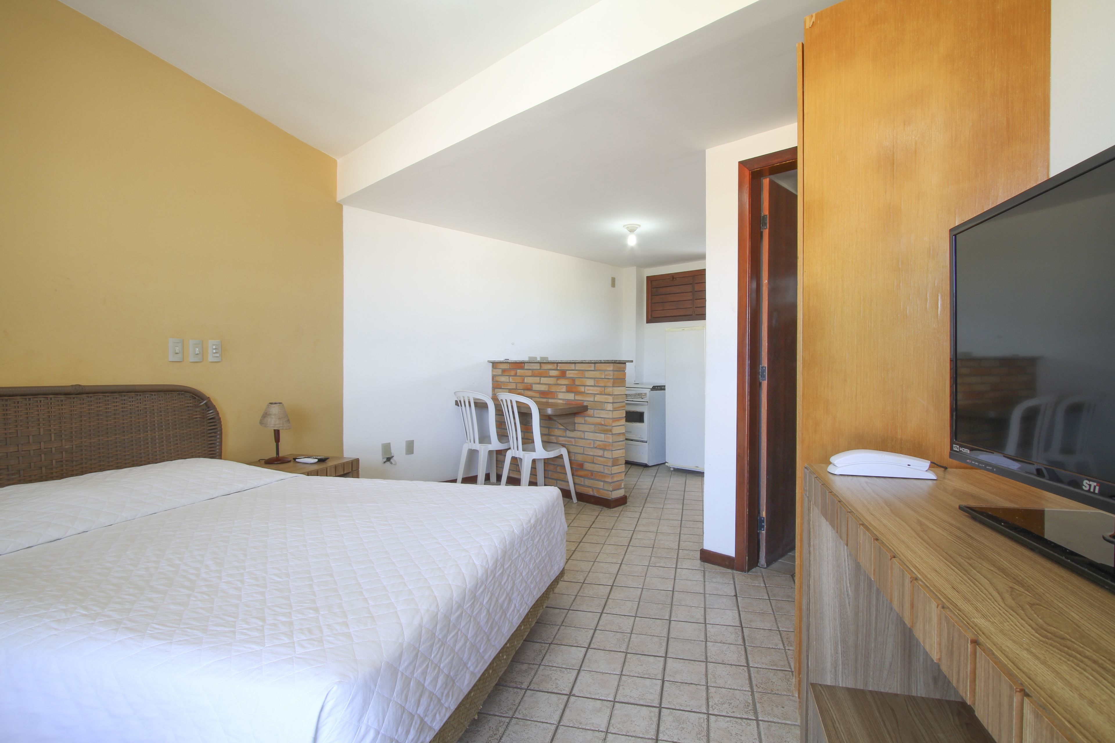 A hotel room with a bed, a TV, a desk, and a small kitchenette.