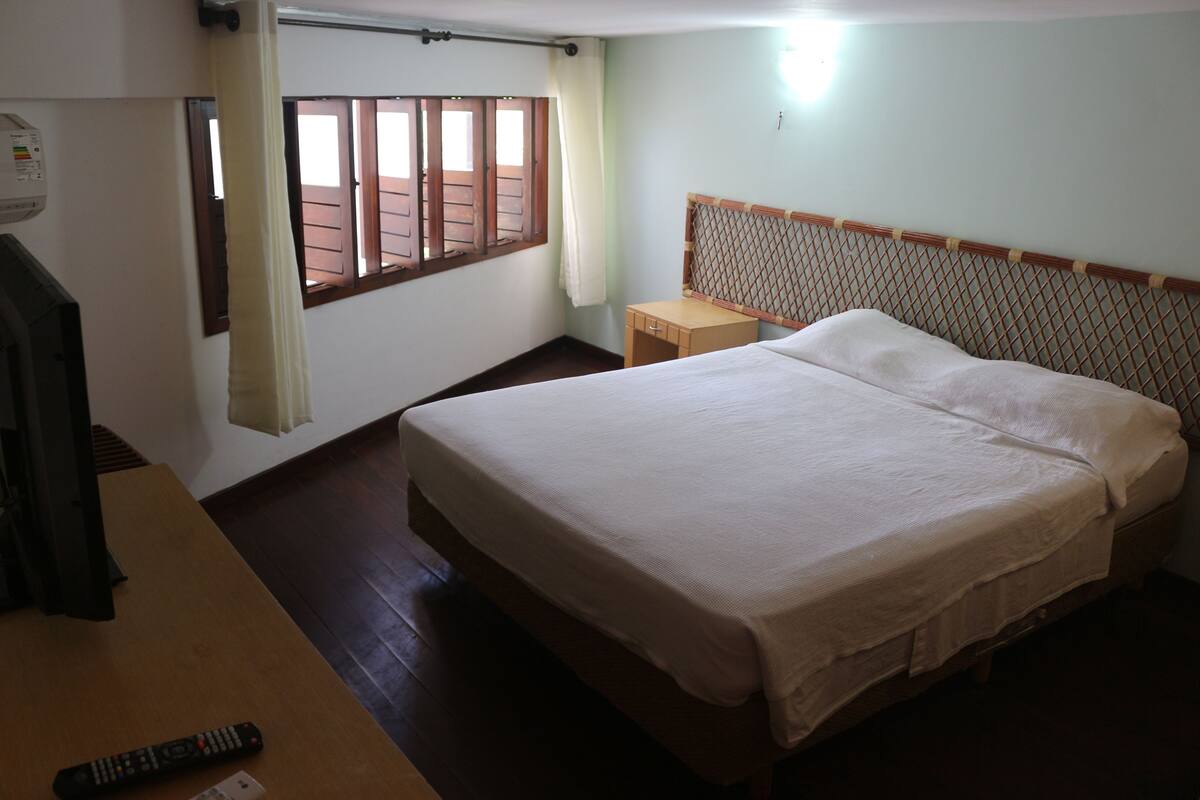 A bedroom with a bed, a nightstand, a television, and a window with curtains.
