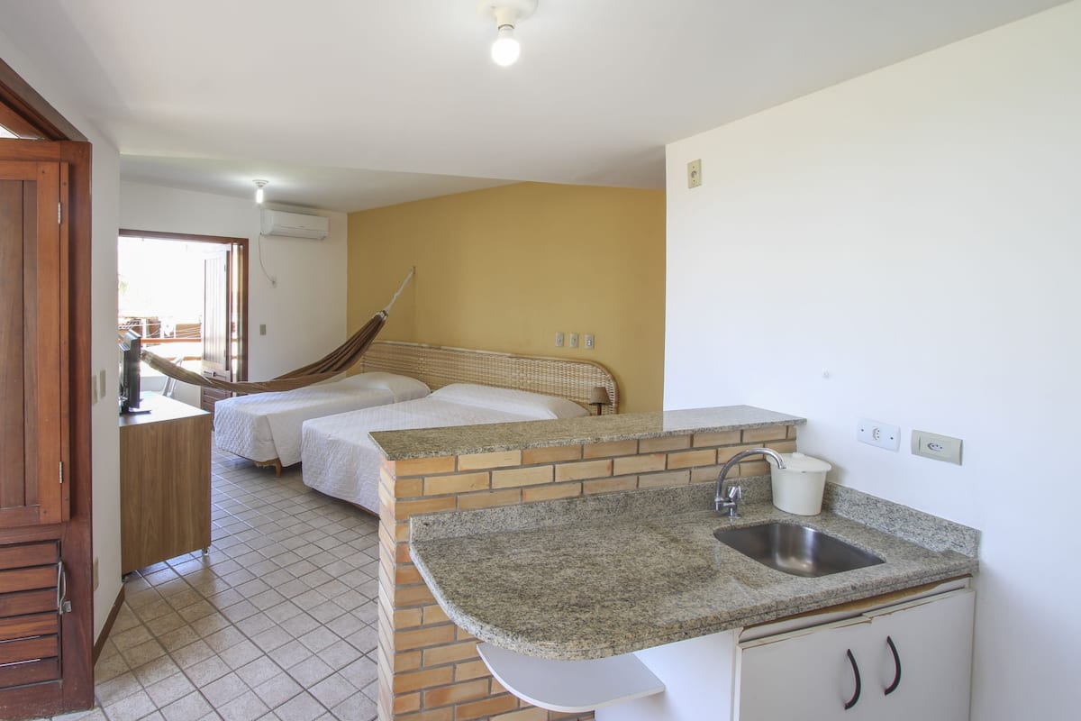 A compact hotel room with a kitchenette, two beds, a small bathroom, and a view of the outside.