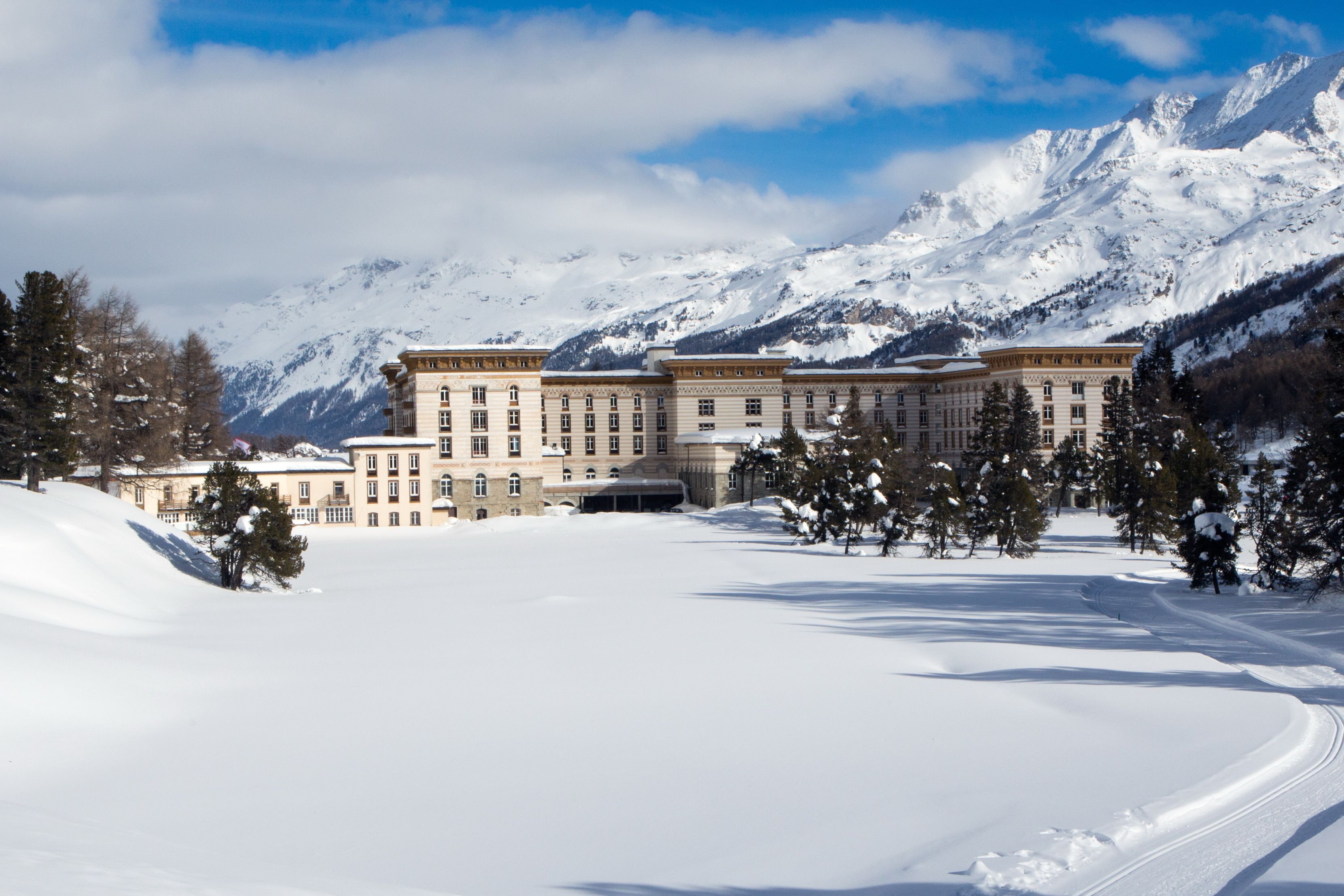 A large, multi-story building with a symmetrical facade, surrounded by snow-covered terrain and mountains in the background.