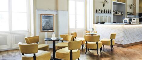 A spacious room with high ceilings, large windows, and a bar area with neatly arranged bottles.