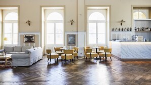 A spacious room with a herringbone wood floor, a white sofa, multiple yellow chairs, a marble bar area, and large arched windows.