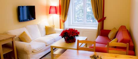 Una sala de estar con un sofá blanco, una mesa de centro de madera, un sofá rojo y naranja, y un televisor montado en la pared.