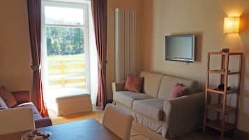 Un salon avec un canapé, une table basse, un téléviseur fixé au mur et une étagère en bois.
