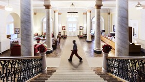A grand lobby with marble columns, a central staircase, and a reception desk.