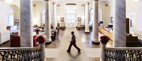 A grand lobby with marble columns, a central staircase, and a reception desk.
