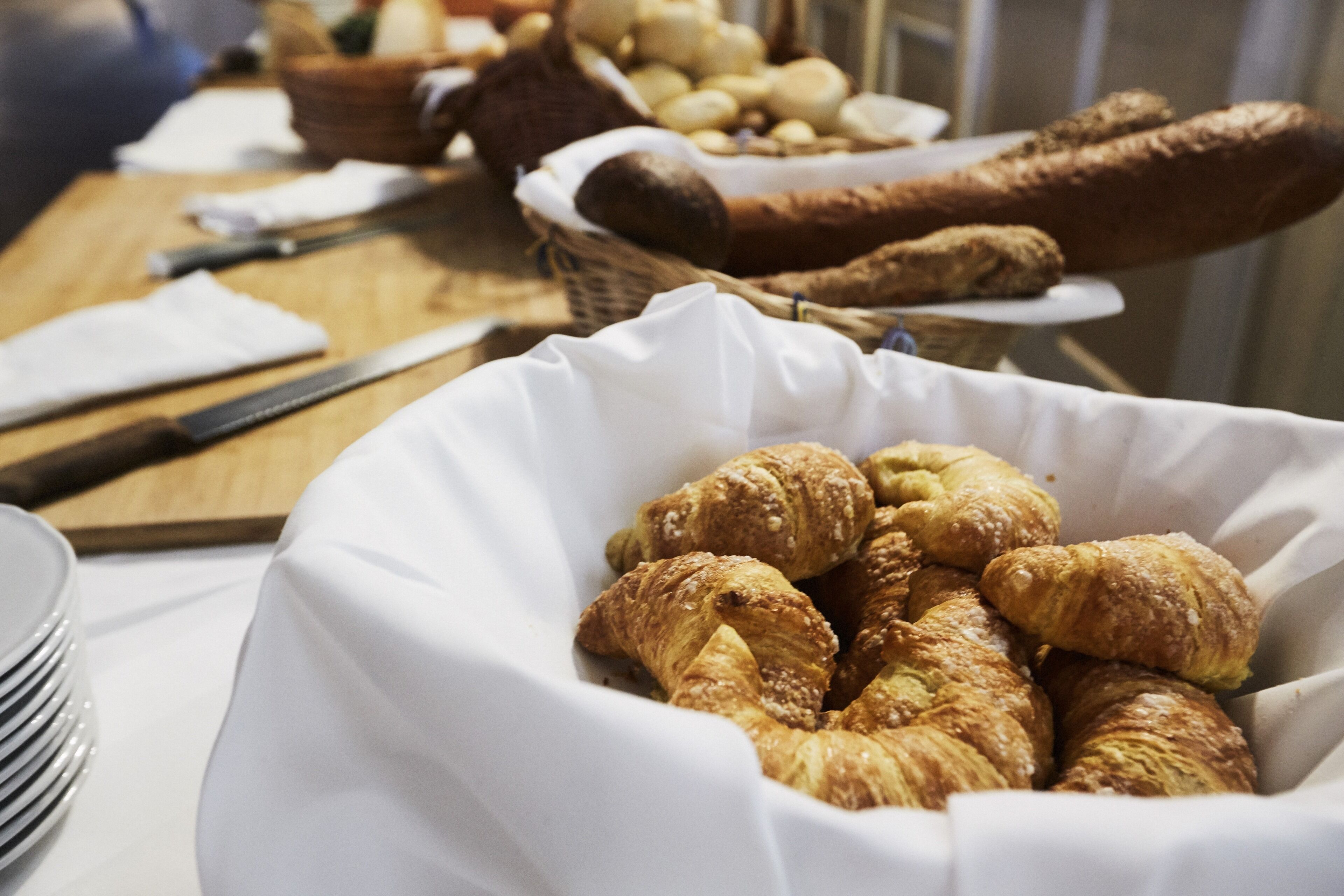 A table with a basket of croissants and a knife.