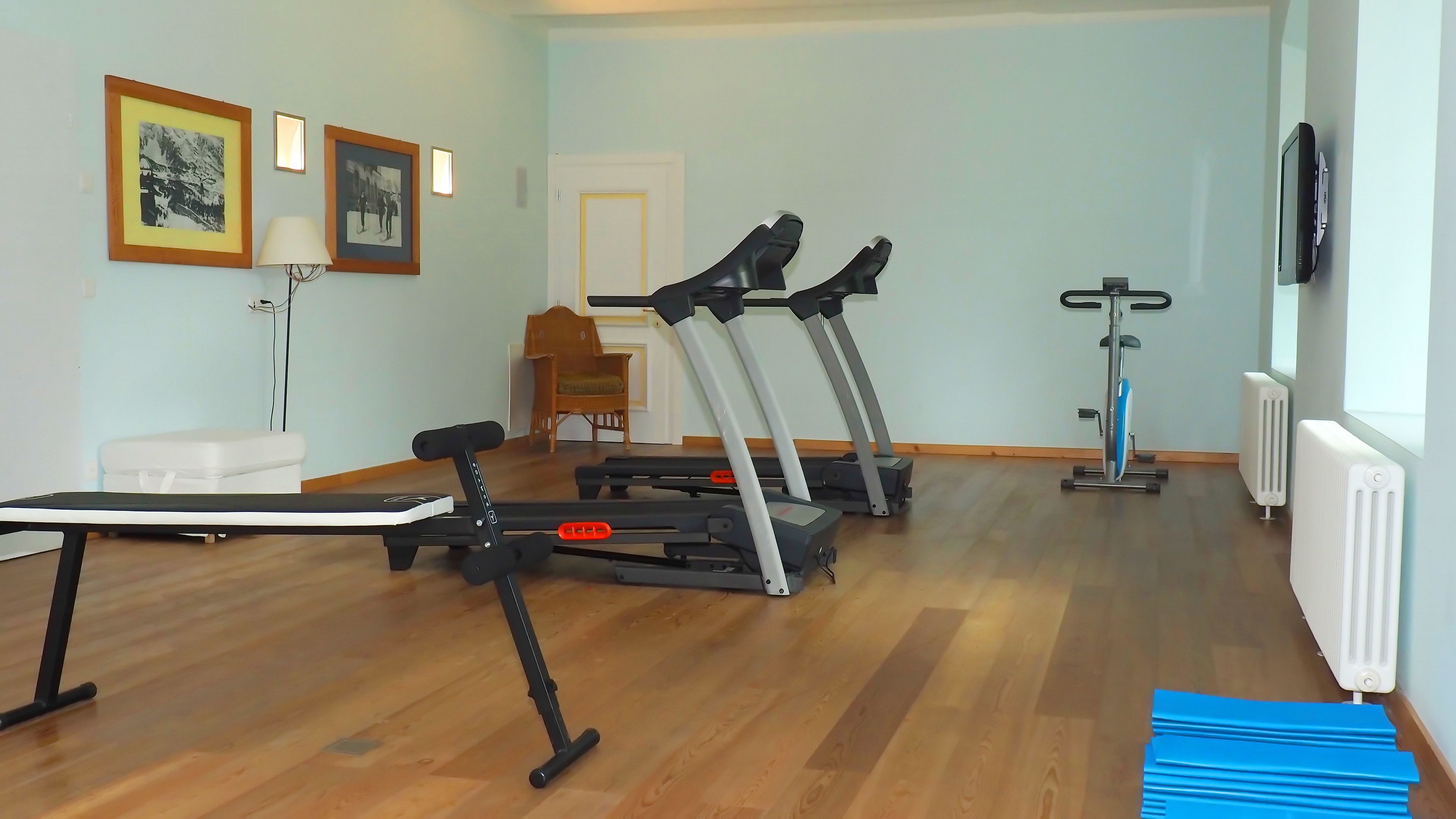 Een huisgym met loopbanden, een hometrainer en een bank.