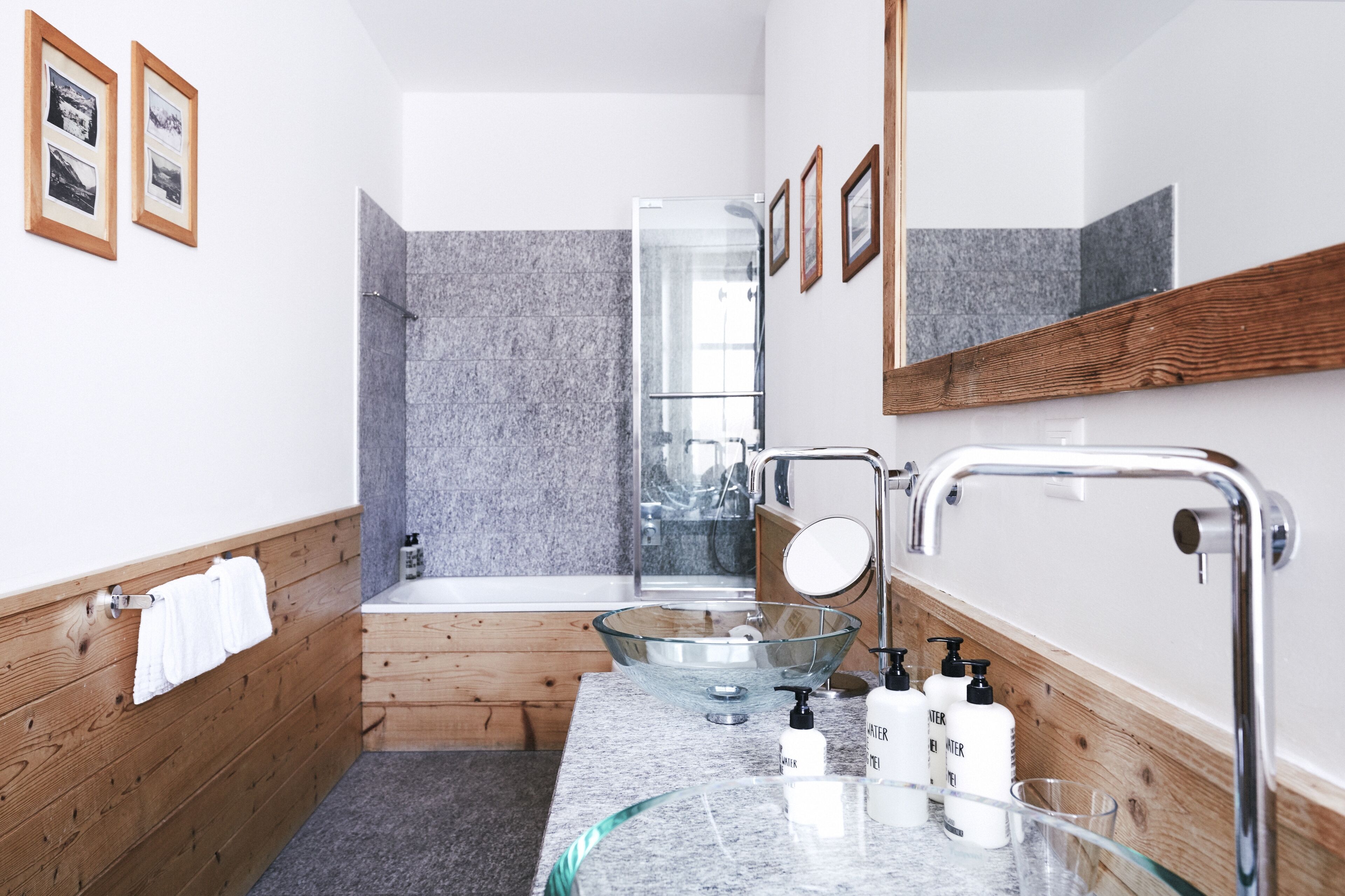A modern bathroom with a glass bowl sink, wooden paneling, a shower, and a large mirror.