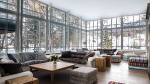 A spacious living room with large windows, a sofa set, ottomans, and a coffee table.