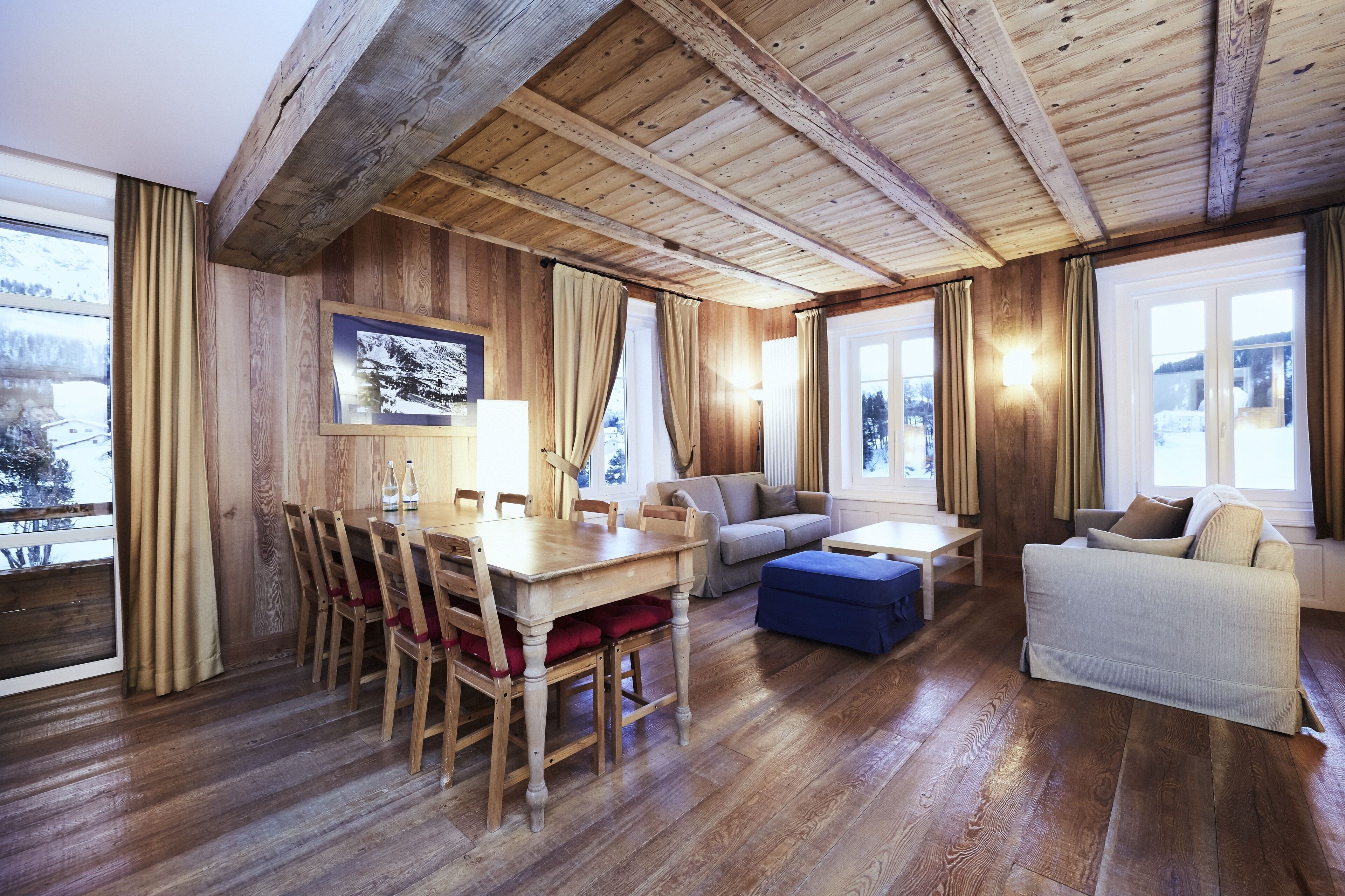 A wooden-floored living room with a dining table, chairs, a sofa, and a couch.