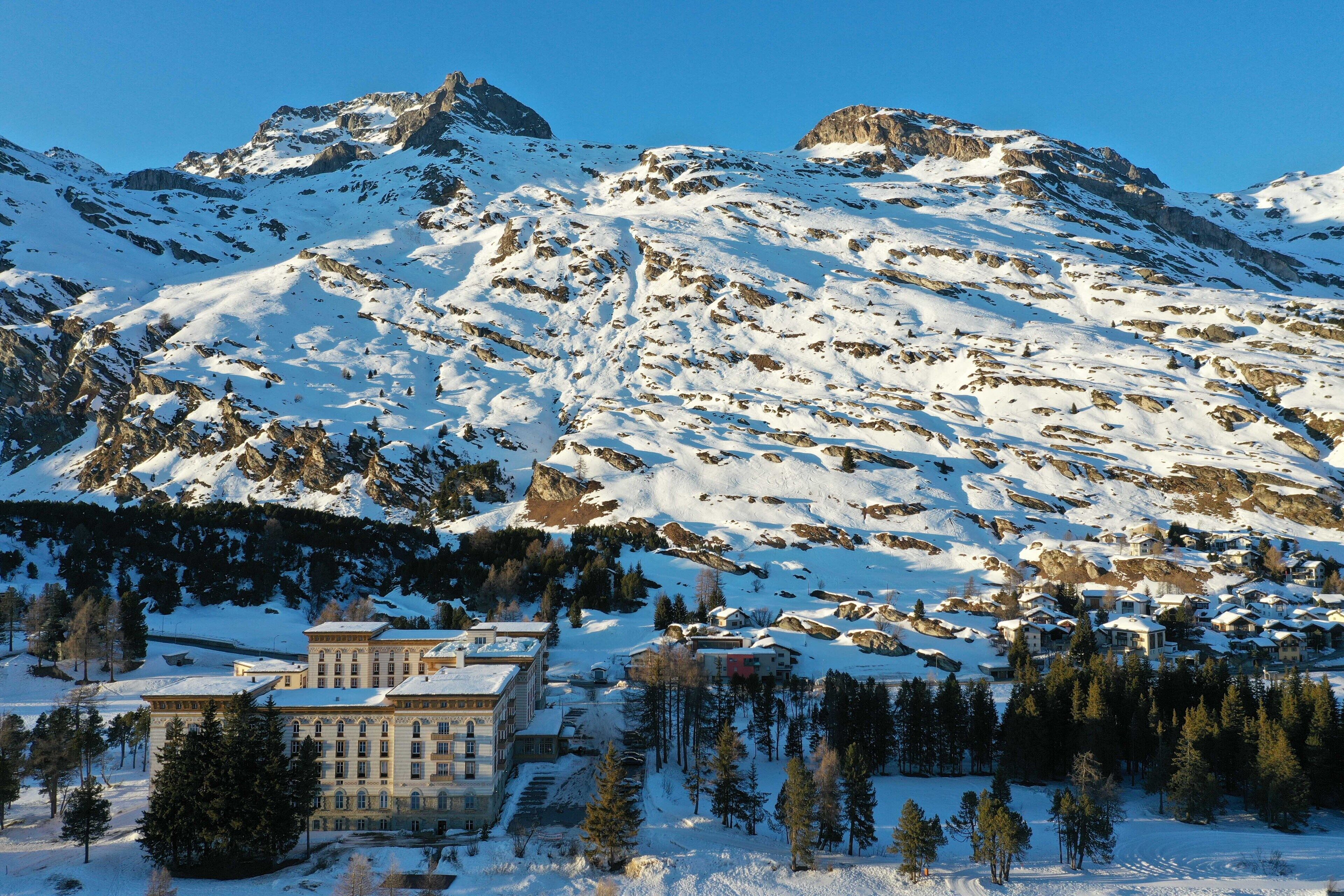Une station de montagne avec des sommets enneigés, un grand bâtiment doté de nombreuses fenêtres et une zone boisée.