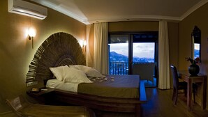 A hotel room with a bed, a wooden chair, a small table, and a view of the city through a large window. - Sandima 37 Suites Hotel (Bodrum)