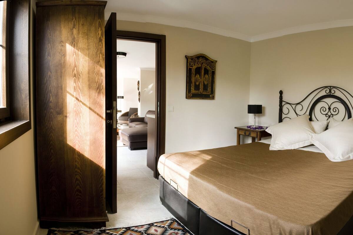 Un dormitorio con una cama grande, dos mesitas de noche, un armario de madera y un espejo decorativo en la pared.