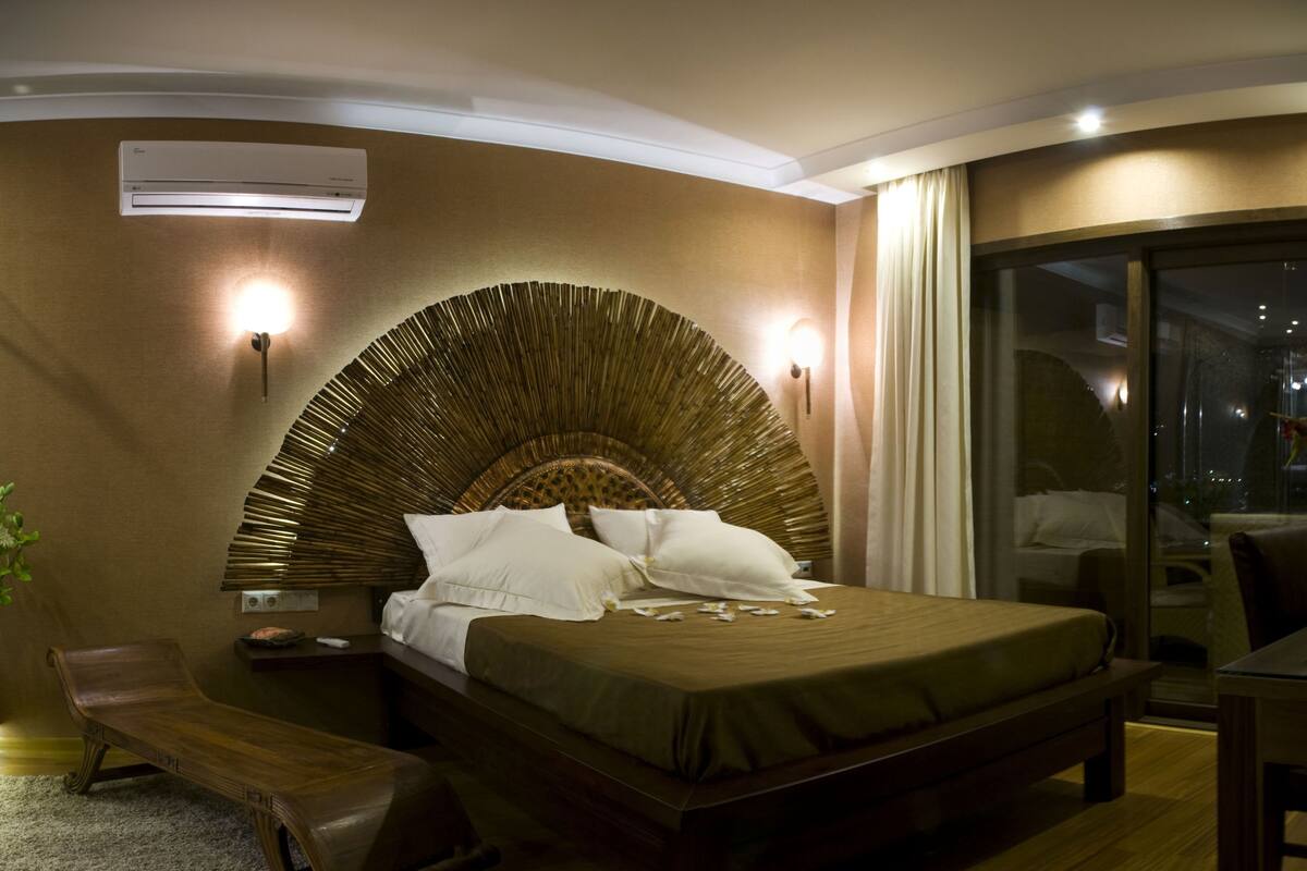 Un dormitorio moderno con cabecera curva, un banco de madera, una mesita de noche y vistas a la ciudad de noche.