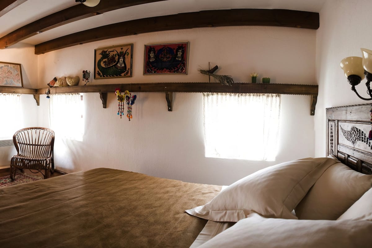 Habitación tradicional con cama, vigas de madera, una silla y detalles decorativos en las paredes.