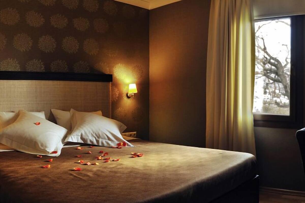 Una habitación de hotel con una cama, dos lámparas de pared y un ventanal con cortinas.