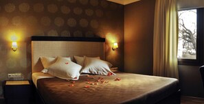Una habitación de hotel con una cama, dos lámparas de pared y un ventanal con cortinas.
