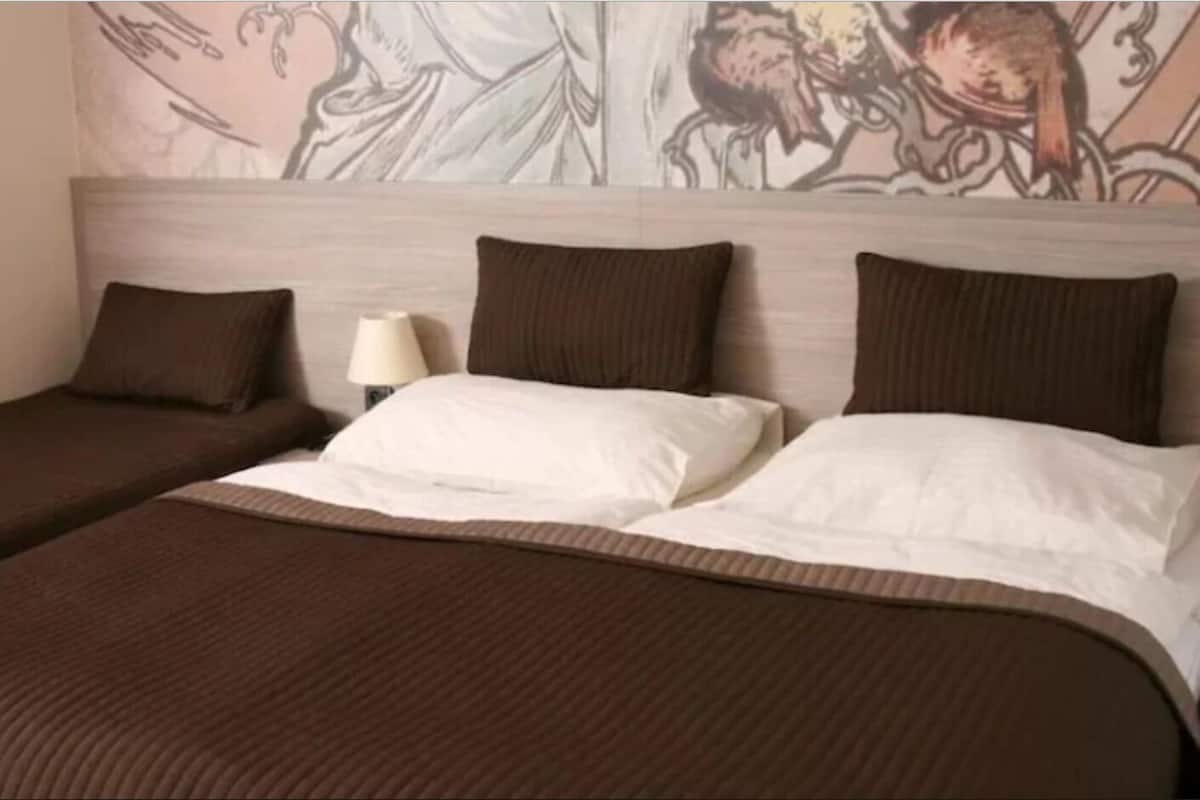 Una habitación de hotel con una cama grande, dos almohadas, una lámpara de noche y un mural en la pared.