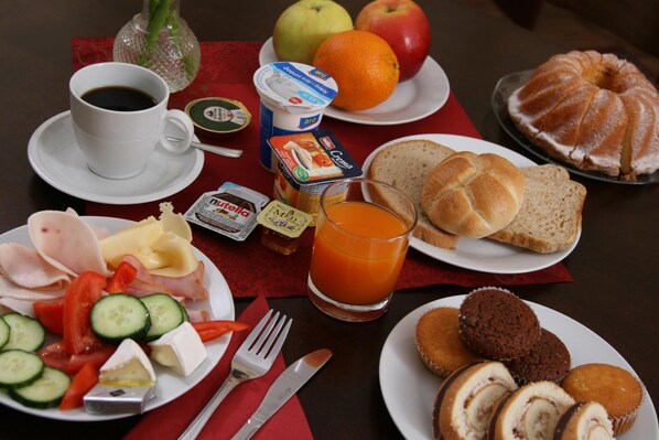 A breakfast table with various food items, including bread, fruits, and a glass of orange juice. - Hotel Klára (Prague)