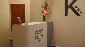 A reception desk at the Klara Hotel with a wooden door, a vase of flowers, and a large 'K' sign on the wall. - Hotel Klára (Prague)