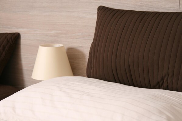 A bed with a white quilted cover, a brown pillow, and a beige lamp beside it. - Hotel Klára (Prague)
