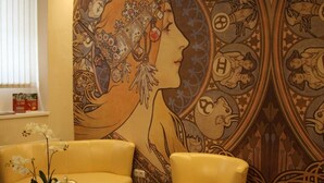 A room with a large mural, yellow chairs, and a table with a bell. - Hotel Klára (Prague)
